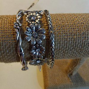 3 silver stretch bracelets with floral pattern on 2 of them.